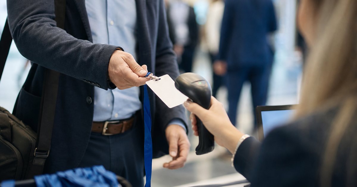 Close-up of a conference attendee holding a lanyard badge up to a handheld scanner at a registration desk, soft lobby lighting, blurred crowd in the background